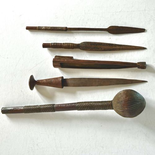 fig 1. A collection of five traditional Zulu artefacts including a fluted knobkerrie club, a wooden dagger with sheath, and two wire-wrapped spearheads on a plain background.