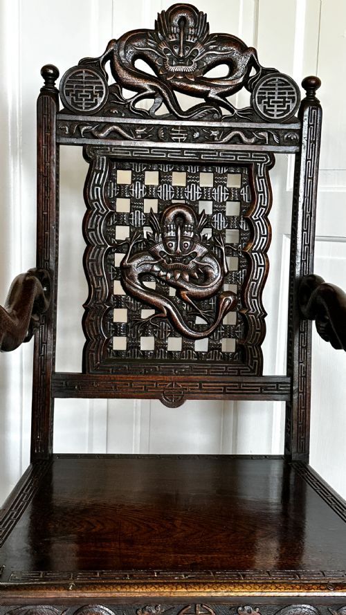 fig 1. A dark brown carved wood armchair featuring openwork lattice panels, carved dragon motifs on the backrest, apron, and stretchers, and carved dragon heads forming the armrests.