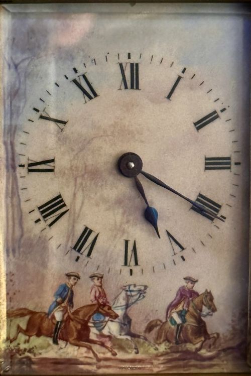 fig 2. A French gilded brass carriage clock featuring an ornate top handle, detailed relief scrollwork borders, and a porcelain dial decorated with an equestrian scene.