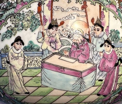 fig 1. A rounded Chinese Famille Rose porcelain bowl decorated with vibrant pink floral enamelling and figural court scenes, resting on a carved dark wooden stand.