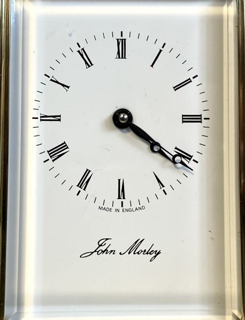 fig 1. A brass carriage clock featuring bevelled glass panels, reeded corner columns, a white dial with Roman numerals, a top carrying handle, and a brass winding key.