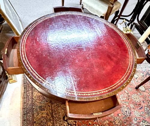 fig 1. A circular antique mahogany drum table featuring a brown leather inset top, painted floral frieze drawers, and a central pedestal base on splayed legs with brass castors.