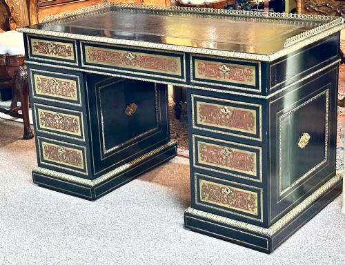 fig 1. An ebonised French pedestal desk featuring red tortoiseshell and brass Boulle marquetry inlay, multiple drawers, a leather writing top, and a brass gallery.