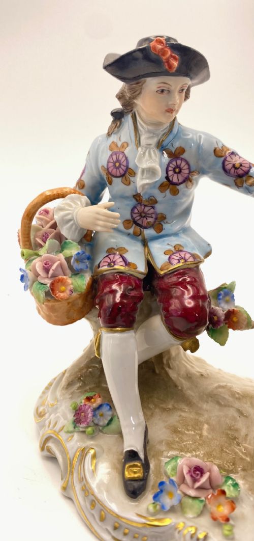 A Sitzendorf porcelain figurine group depicting an 18th-century courtly couple seated together with flower baskets on a scrollwork base with gold detailing. View III