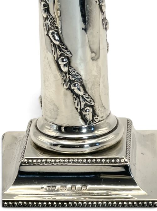 A pair of polished silver column candlesticks featuring Corinthian capitals, foliate swags, and stepped beaded bases. View VII