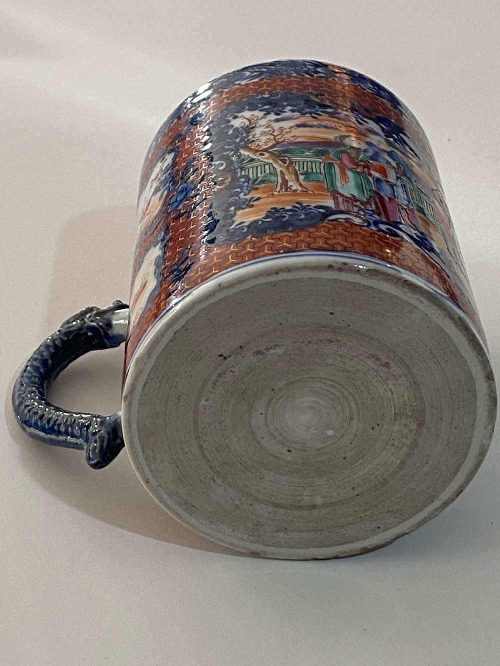 An 18th-century cylindrical Chinese export porcelain tankard decorated with Mandarin figures, panels of birds, iron-red lattice background, and a sculpted blue dragon handle. View VI