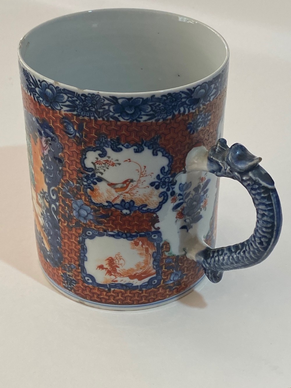 An 18th-century cylindrical Chinese export porcelain tankard decorated with Mandarin figures, panels of birds, iron-red lattice background, and a sculpted blue dragon handle. View VIII