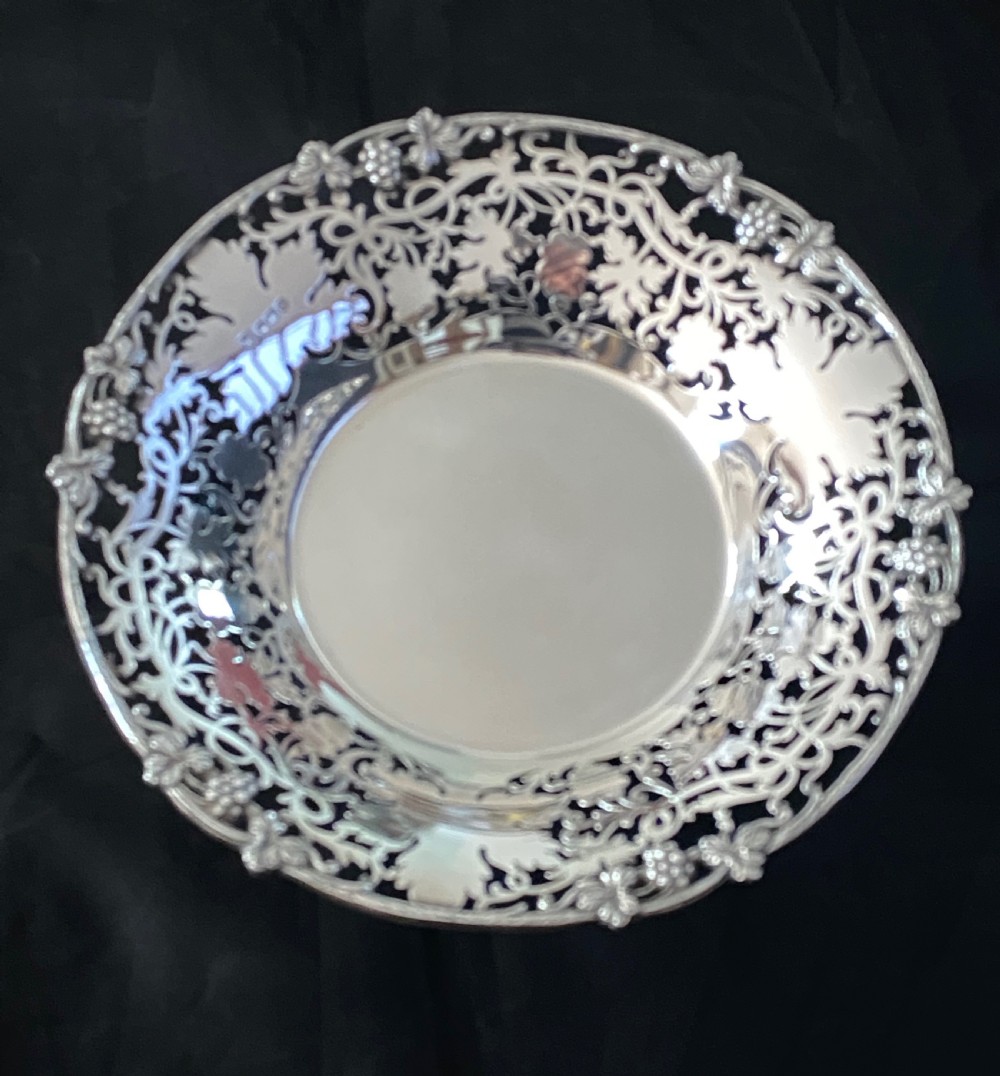 A circular antique silver footed bowl featuring an intricate pierced fretwork rim decorated with grapevine leaves and grape clusters surrounding a smooth polished centre. View III