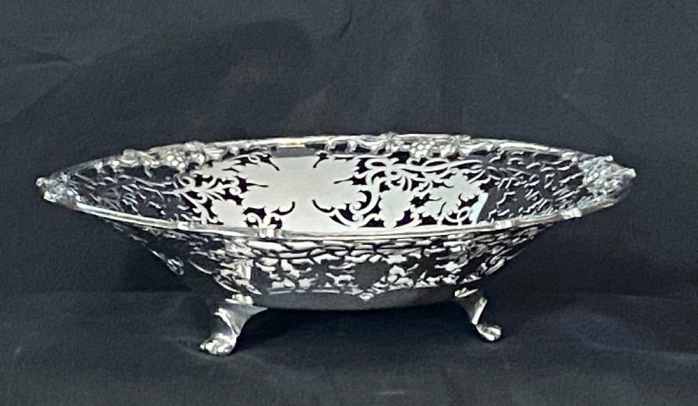 A circular antique silver footed bowl featuring an intricate pierced fretwork rim decorated with grapevine leaves and grape clusters surrounding a smooth polished centre. View II