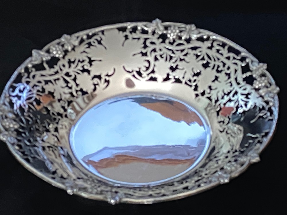 A circular antique silver footed bowl featuring an intricate pierced fretwork rim decorated with grapevine leaves and grape clusters surrounding a smooth polished centre. View XV