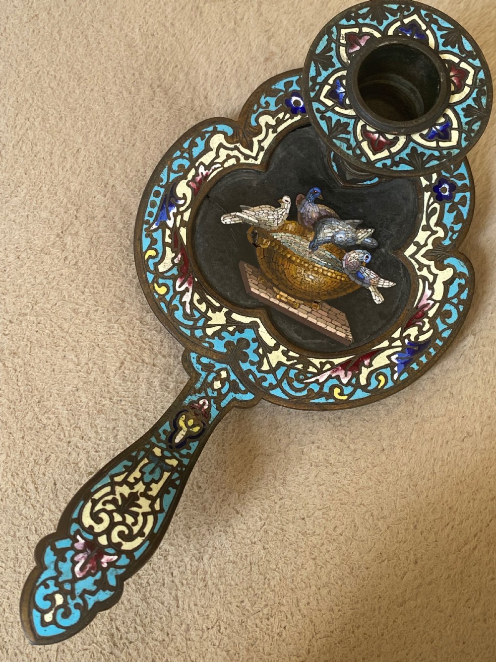 An antique metal chamberstick decorated with turquoise cloisonne enamel scrollwork surrounding a central micromosaic panel of birds drinking from a bowl.
