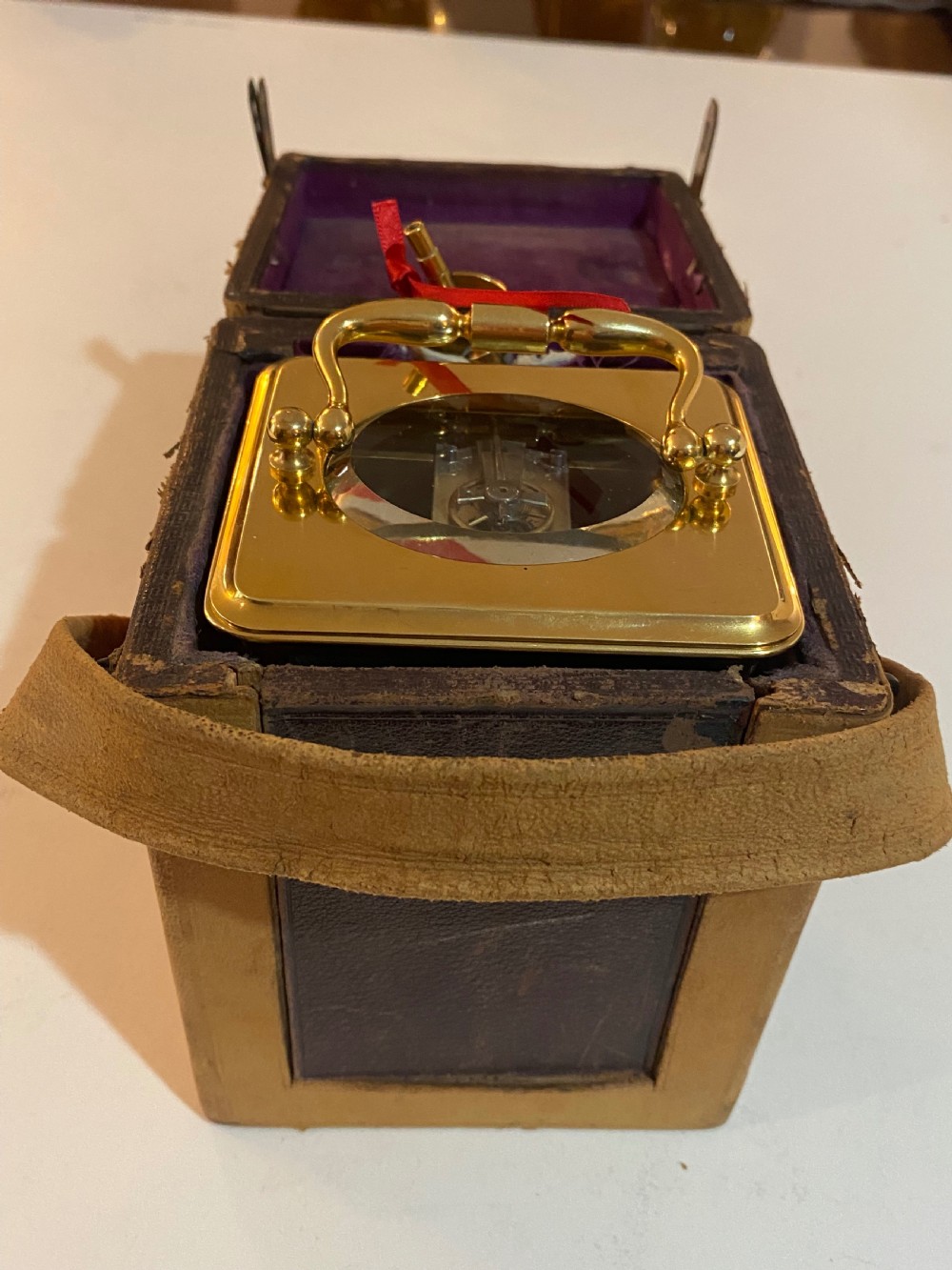 A rectangular gilt brass carriage clock featuring a folding top handle, white enamel dial with Roman numerals, and a lower auxiliary alarm dial. View X