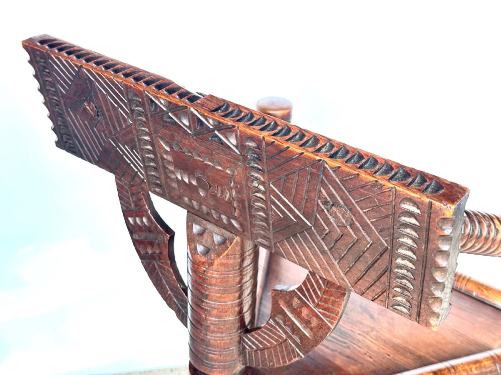 A dark oak three-legged turned chair featuring a triangular wooden seat, turned spindle arms, bobbin legs, and a carved geometric backrest panel. View VIII