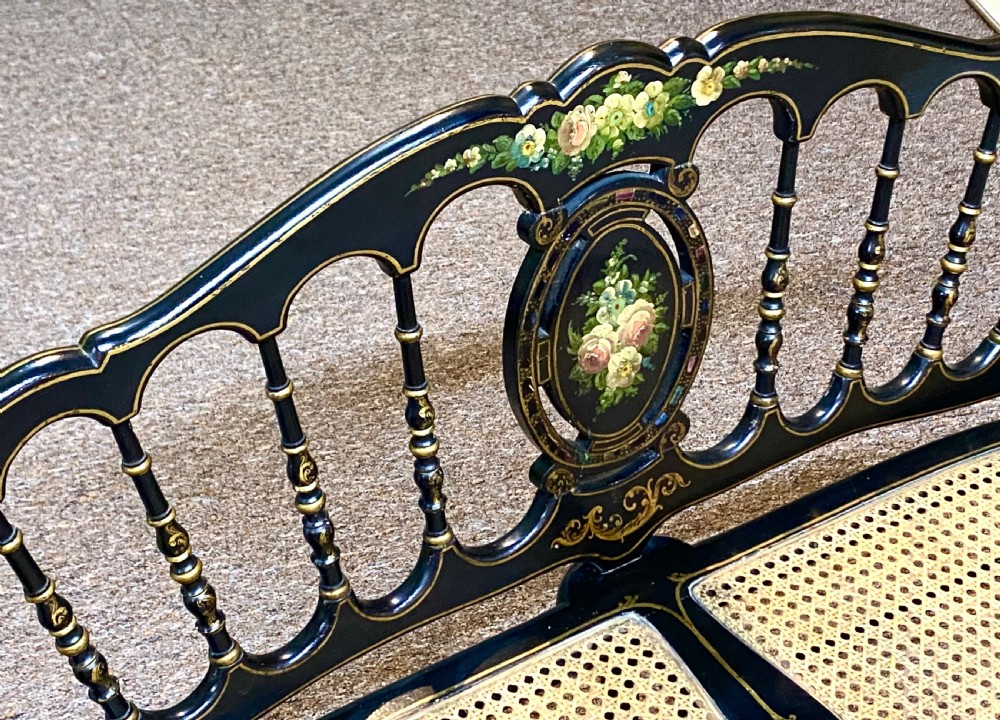 An antique black ebonised wooden bench with hand-painted floral panels, gold accents, turned spindle backrest, and two cane seat panels. View III
