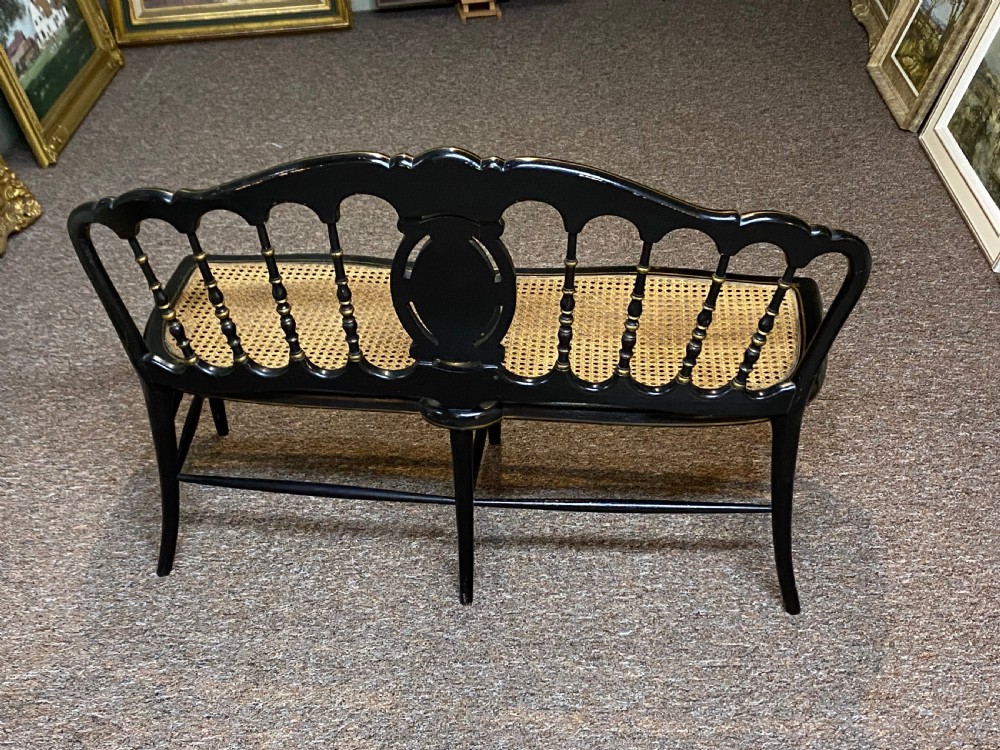 An antique black ebonised wooden bench with hand-painted floral panels, gold accents, turned spindle backrest, and two cane seat panels. View IV