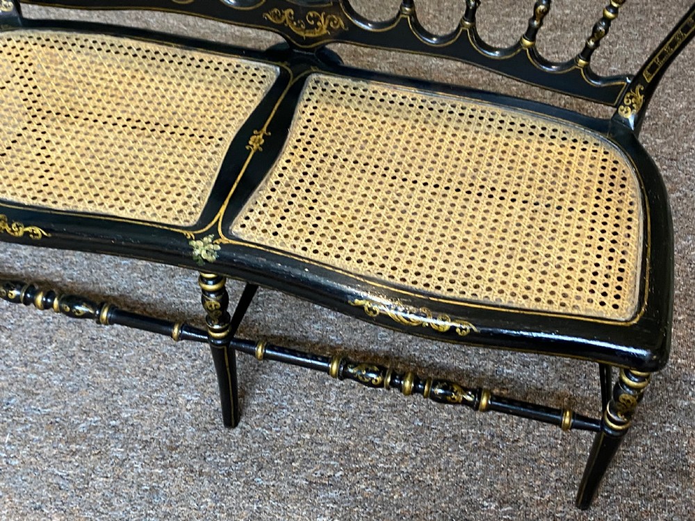 An antique black ebonised wooden bench with hand-painted floral panels, gold accents, turned spindle backrest, and two cane seat panels. View VI