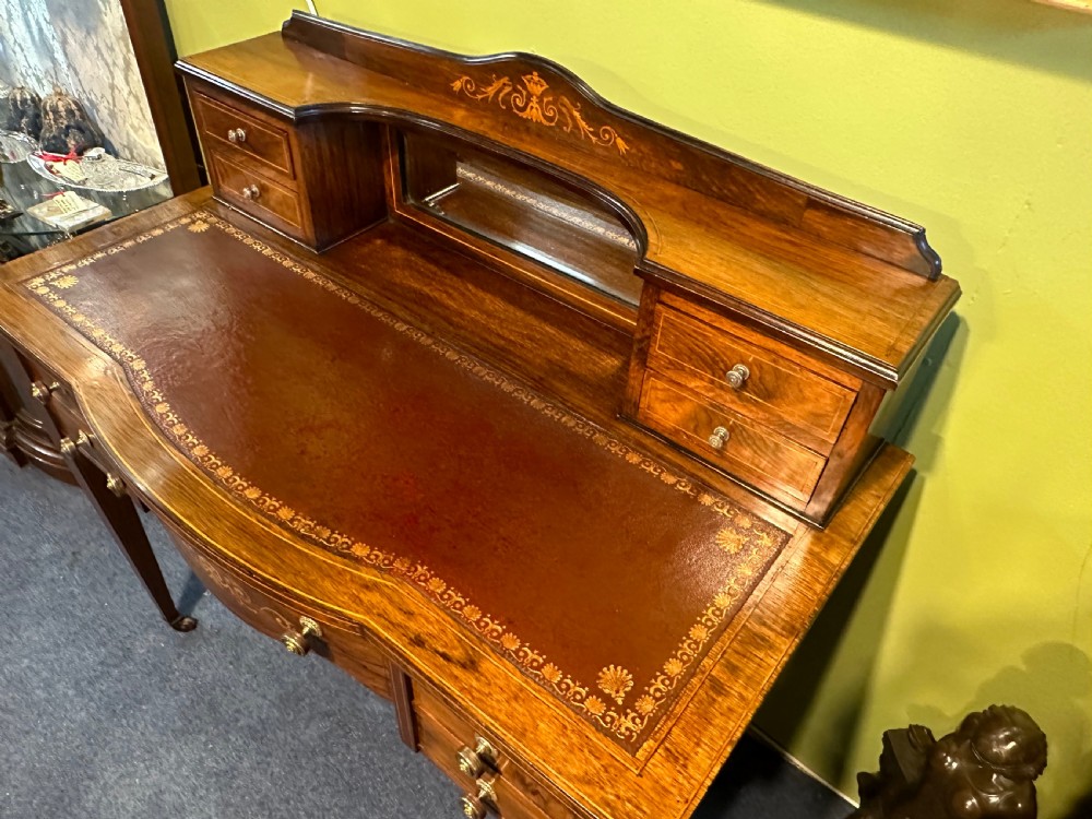 An Edwardian rosewood writing desk with satinwood marquetry, a dark brown leather writing surface, a raised superstructure with small drawers and a mirror, standing on tapered legs with castors. View IV