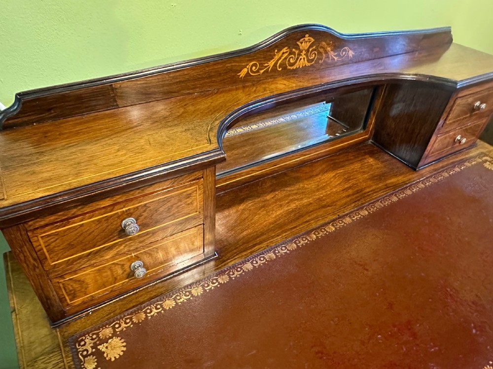 An Edwardian rosewood writing desk with satinwood marquetry, a dark brown leather writing surface, a raised superstructure with small drawers and a mirror, standing on tapered legs with castors. View V
