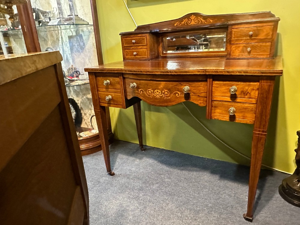 An Edwardian rosewood writing desk with satinwood marquetry, a dark brown leather writing surface, a raised superstructure with small drawers and a mirror, standing on tapered legs with castors. View VII