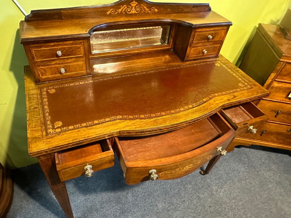 An Edwardian rosewood writing desk with satinwood marquetry, a dark brown leather writing surface, a raised superstructure with small drawers and a mirror, standing on tapered legs with castors. View VIII