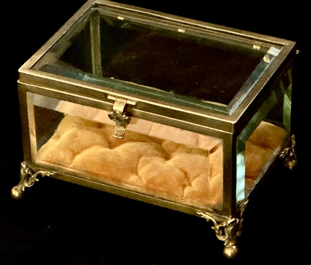 A rectangular French glass trinket box featuring a gilded ormolu frame, bevelled glass panels, decorative cast feet, and a tufted tan velvet cushion inside. View II