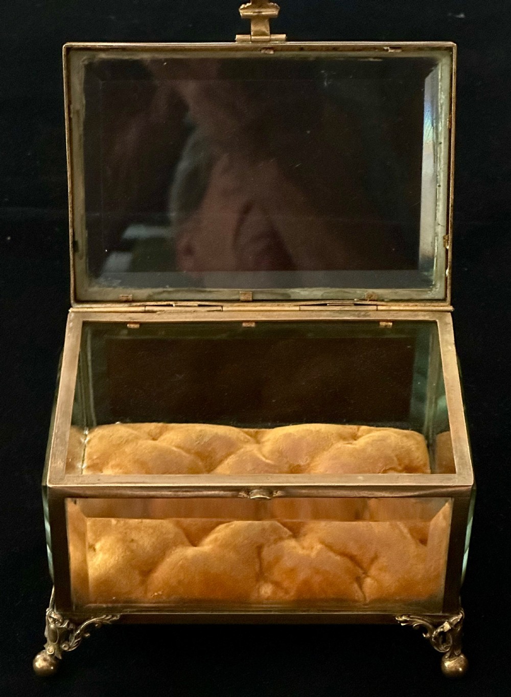 A rectangular French glass trinket box featuring a gilded ormolu frame, bevelled glass panels, decorative cast feet, and a tufted tan velvet cushion inside. View V