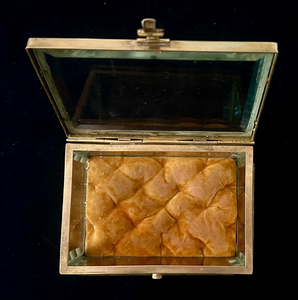 A rectangular French glass trinket box featuring a gilded ormolu frame, bevelled glass panels, decorative cast feet, and a tufted tan velvet cushion inside. View VI
