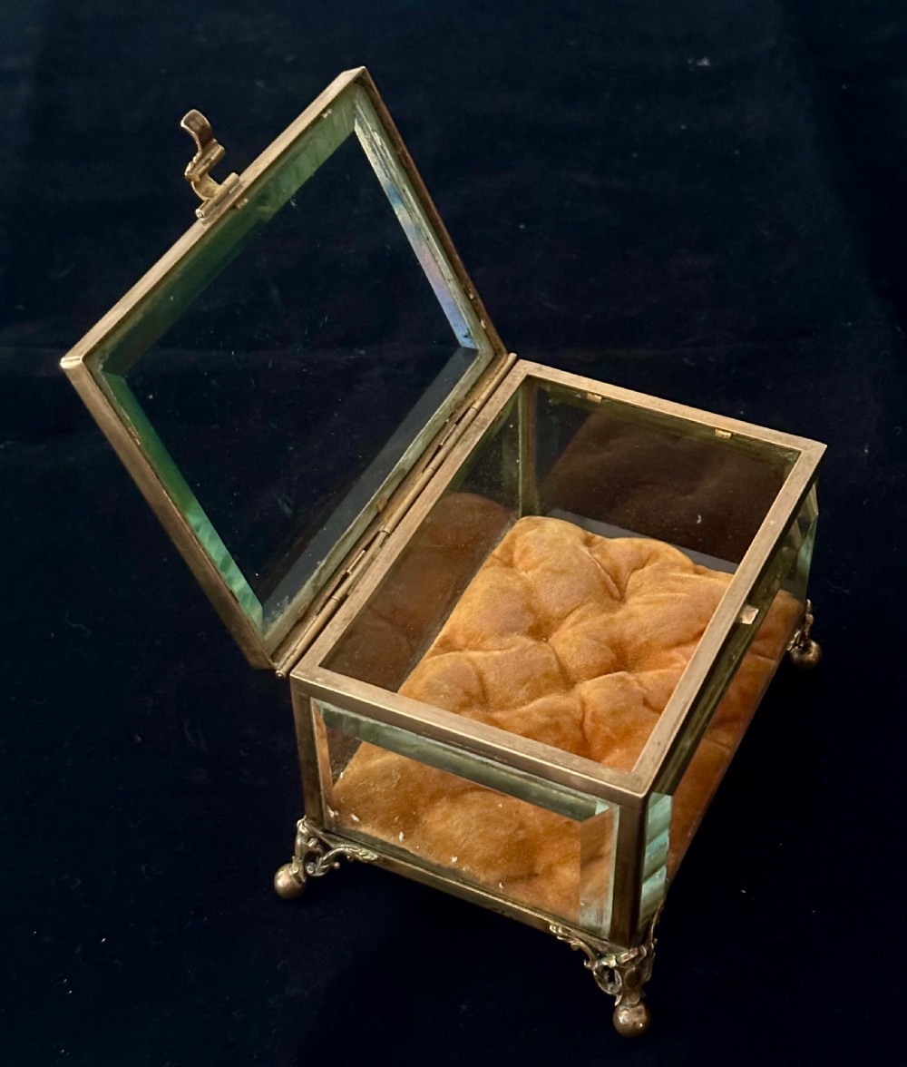 A rectangular French glass trinket box featuring a gilded ormolu frame, bevelled glass panels, decorative cast feet, and a tufted tan velvet cushion inside. View VII