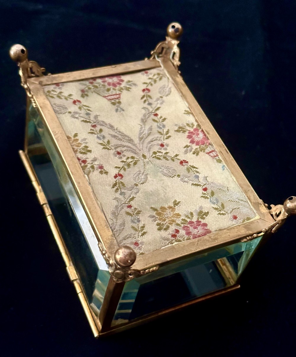 A rectangular French glass trinket box featuring a gilded ormolu frame, bevelled glass panels, decorative cast feet, and a tufted tan velvet cushion inside. View IX
