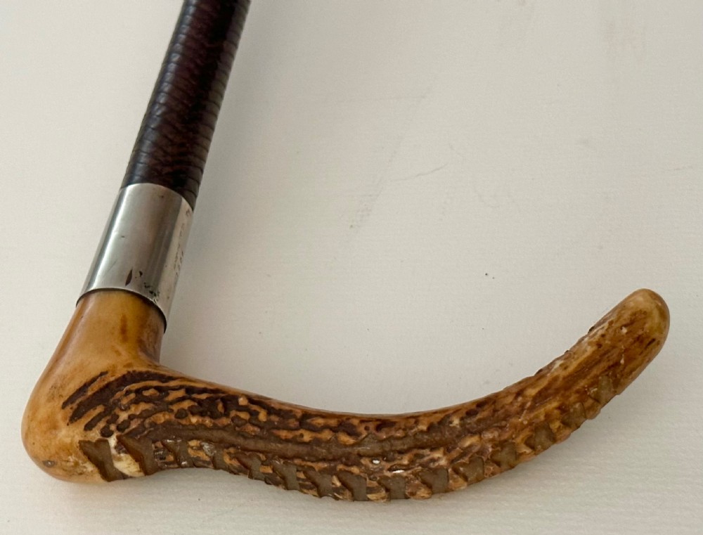 An antique riding crop featuring a carved antler handle, a silver collar, a dark woven shaft, and a braided leather lash. View IV