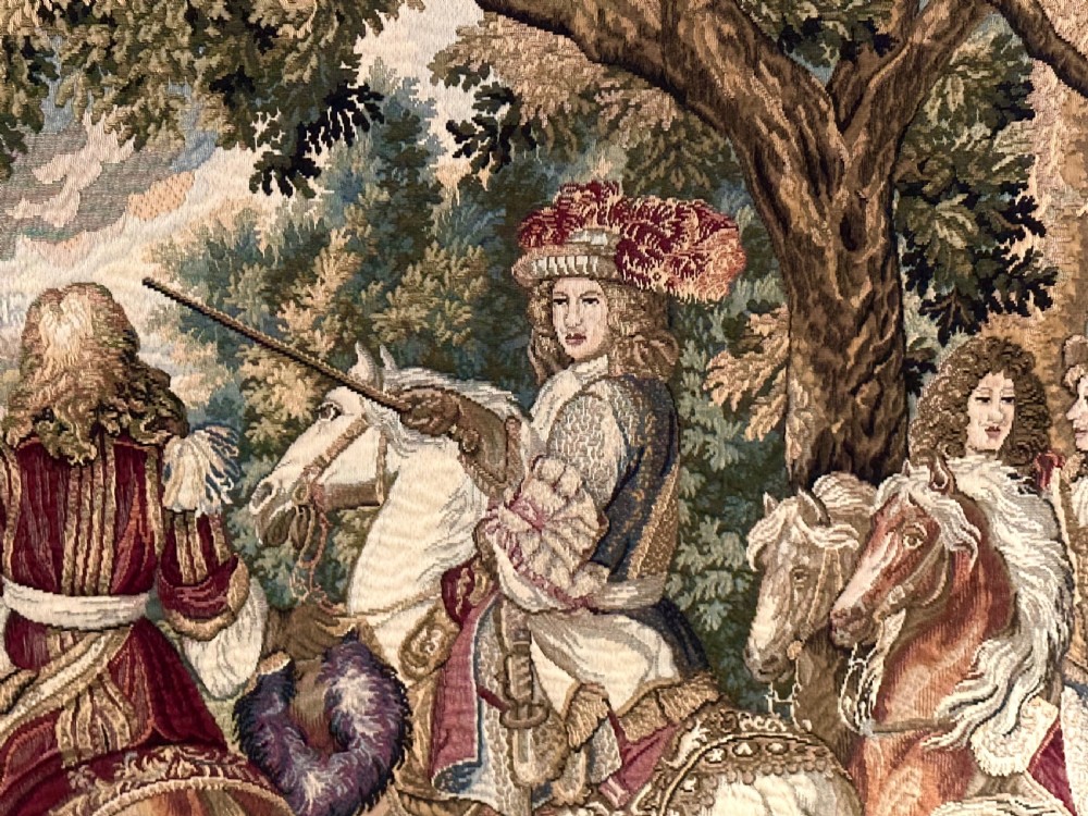 A large needlework wall tapestry featuring a French battle scene with cavalry figures enclosed by a detailed floral border and heraldic crest. View V