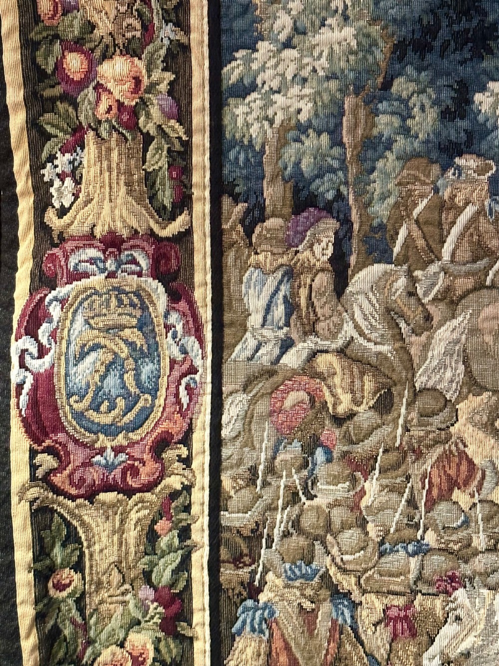 A large needlework wall tapestry featuring a French battle scene with cavalry figures enclosed by a detailed floral border and heraldic crest. View VIII