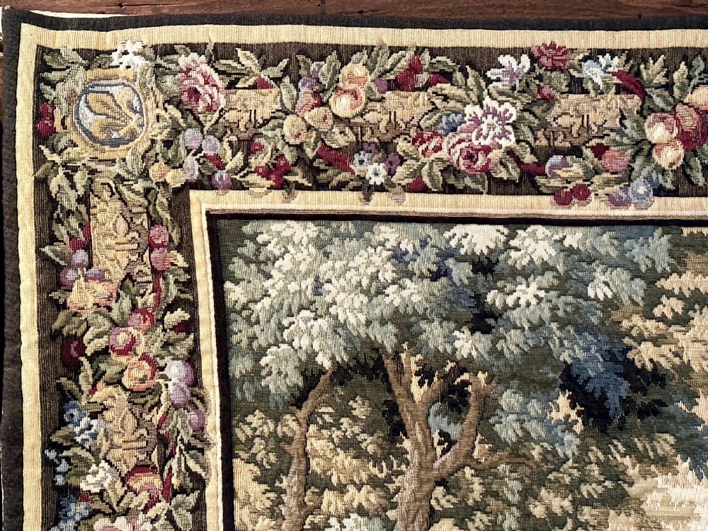 A large needlework wall tapestry featuring a French battle scene with cavalry figures enclosed by a detailed floral border and heraldic crest. View IX