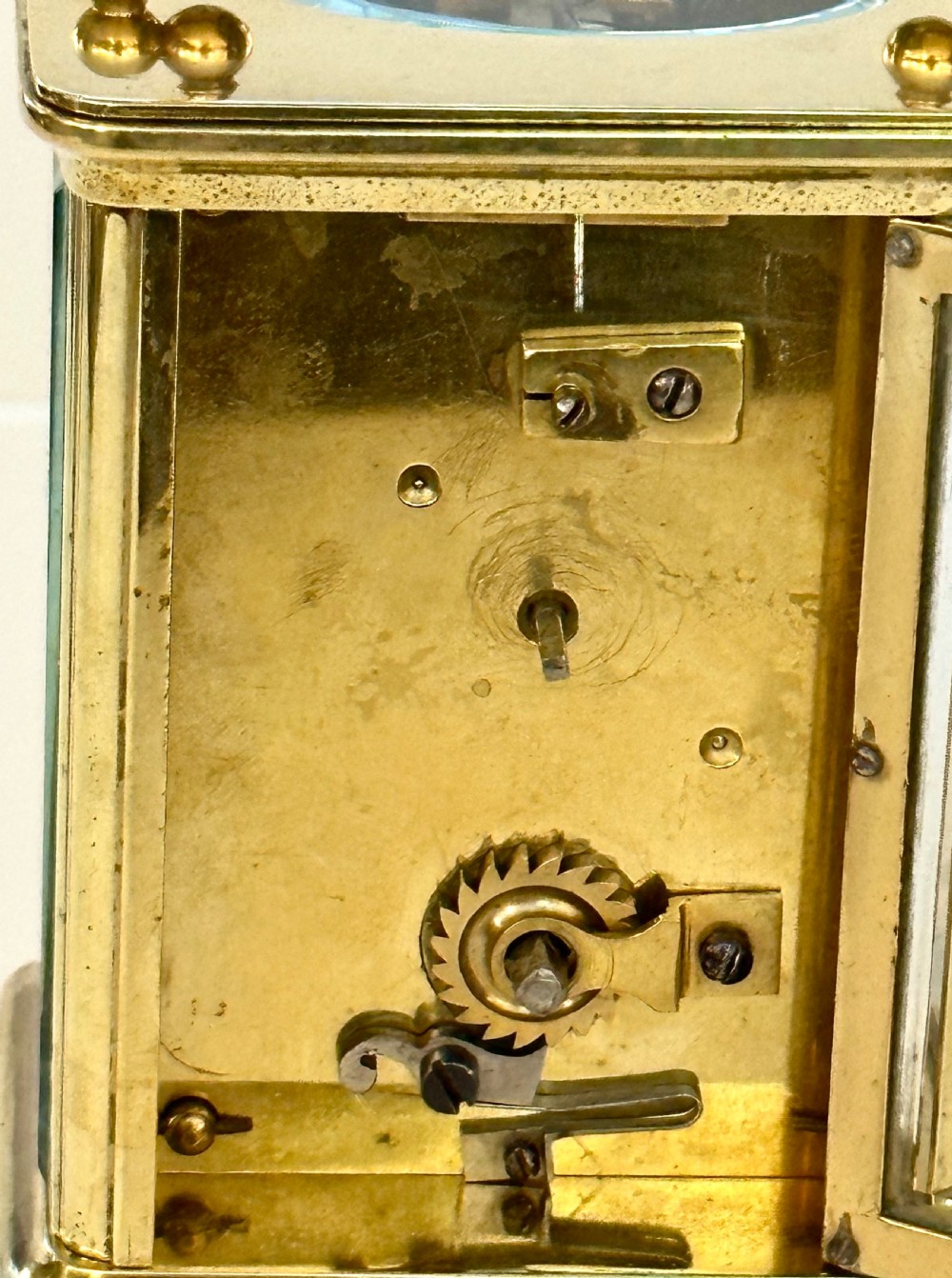 A rectangular brass French carriage clock featuring a white enamel dial with Roman numerals, black hands, bevelled glass sides, and a hinged carrying handle on top. View V