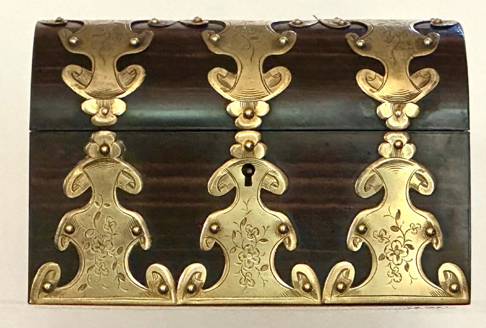 A dark coromandel wood stationery box featuring a domed lid decorated with engraved brass strapwork mounts and a central keyhole.