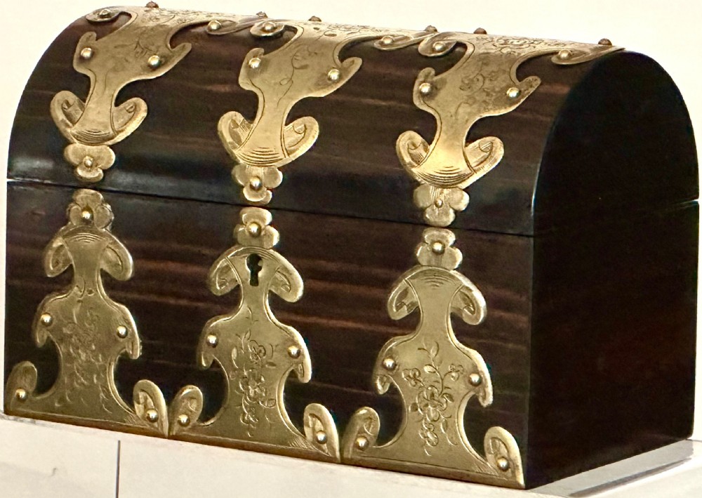 A dark coromandel wood stationery box featuring a domed lid decorated with engraved brass strapwork mounts and a central keyhole. View II