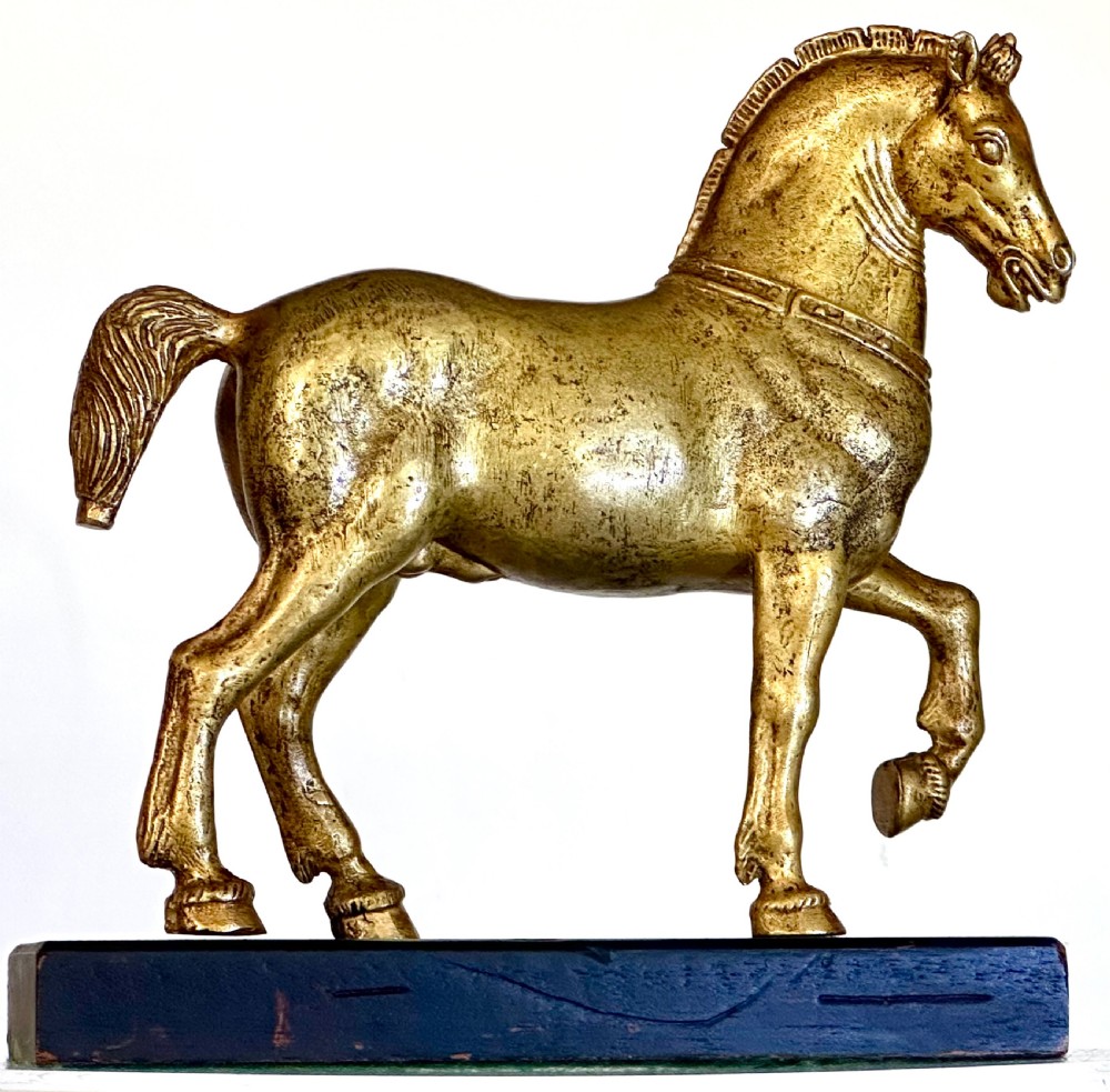 A gilded bronze horse sculpture in a striding pose with one raised hoof, mounted on a dark rectangular base.