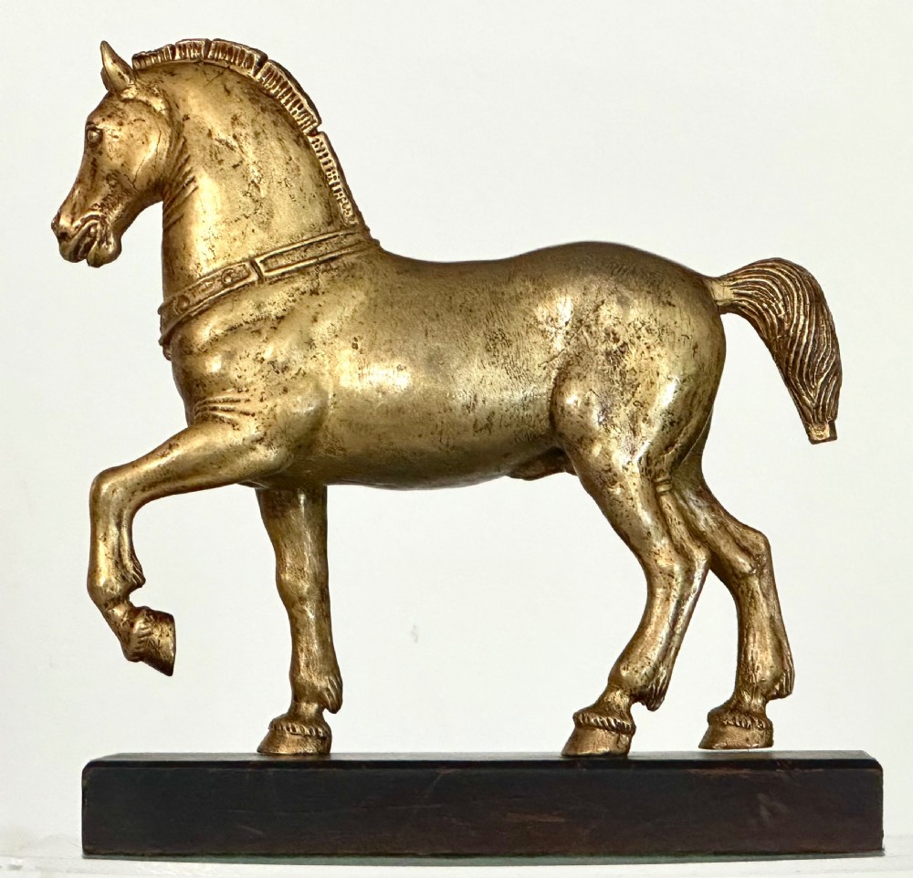A gilded bronze horse sculpture in a striding pose with one raised hoof, mounted on a dark rectangular base. View IV
