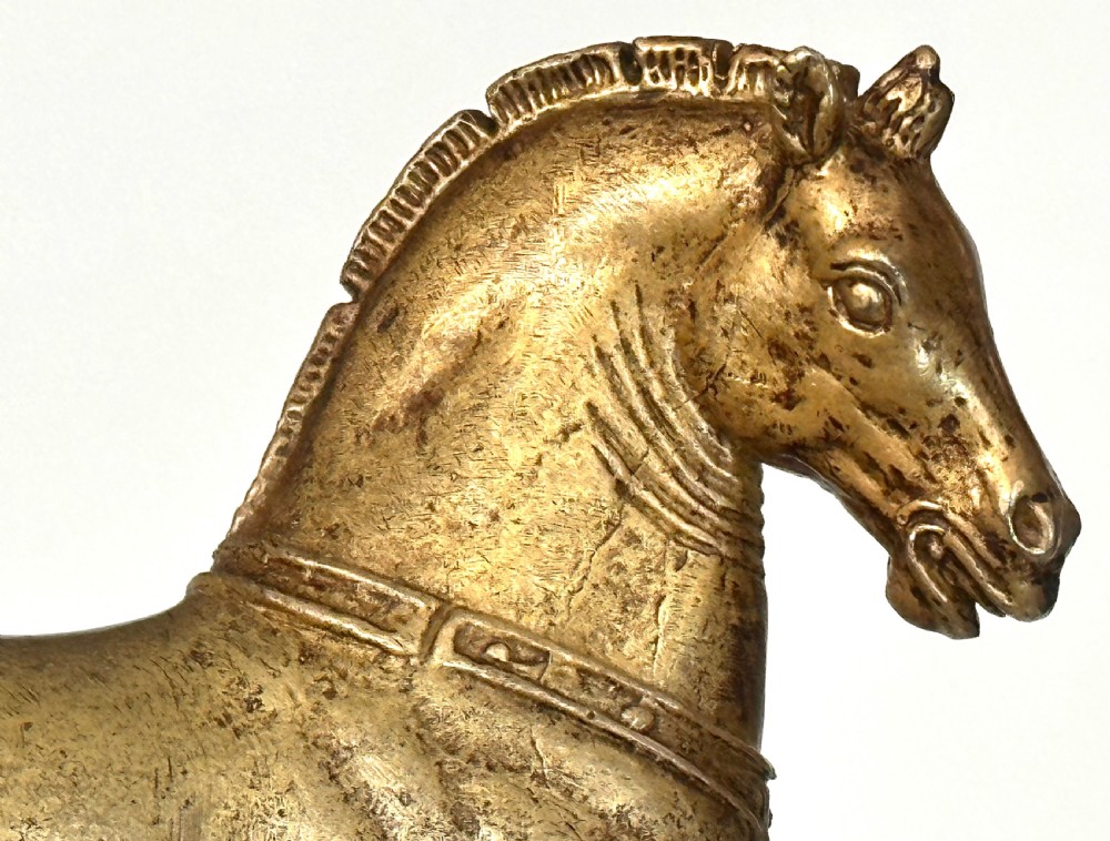 A gilded bronze horse sculpture in a striding pose with one raised hoof, mounted on a dark rectangular base. View V