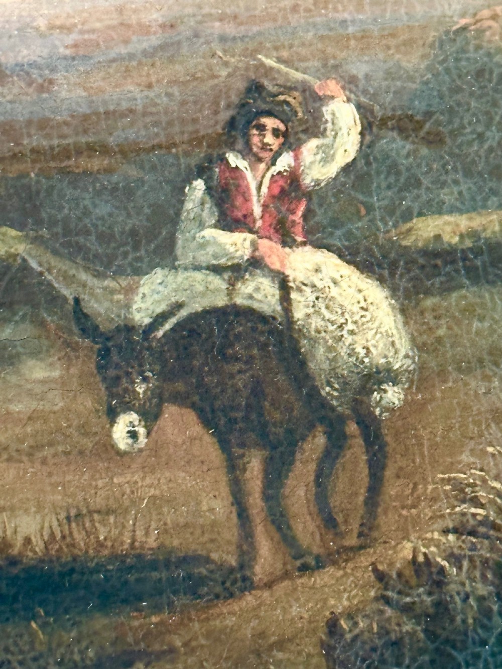 An 18th-century oil painting on canvas depicting a rural landscape with a stone gatehouse, a figure riding a donkey, and a warm sunset sky, set within an ornate carved gold gilt frame. View V
