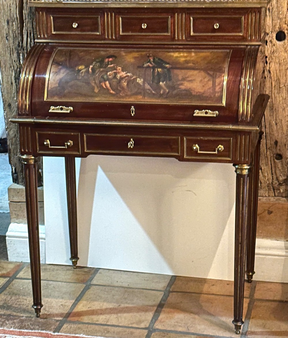 A mahogany French cylinder escritoire featuring a central painted pastoral scene on the roll-top, upper drawer tier, brass mounts, and slender fluted legs.