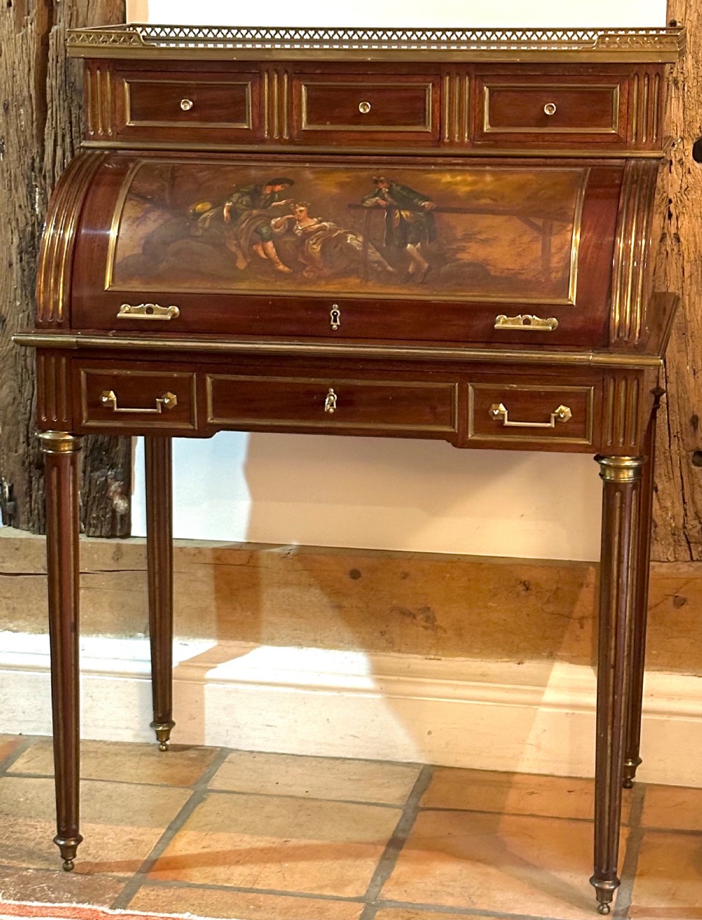 A mahogany French cylinder escritoire featuring a central painted pastoral scene on the roll-top, upper drawer tier, brass mounts, and slender fluted legs. View II
