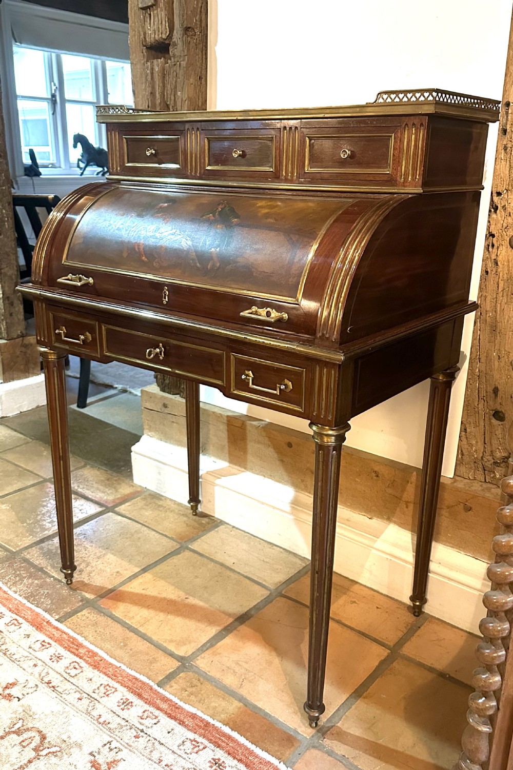 A mahogany French cylinder escritoire featuring a central painted pastoral scene on the roll-top, upper drawer tier, brass mounts, and slender fluted legs. View III