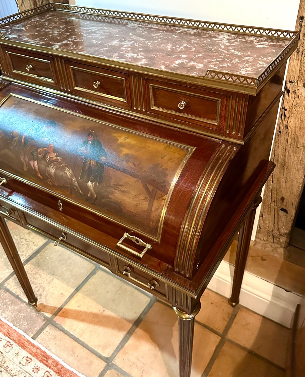 A mahogany French cylinder escritoire featuring a central painted pastoral scene on the roll-top, upper drawer tier, brass mounts, and slender fluted legs. View V