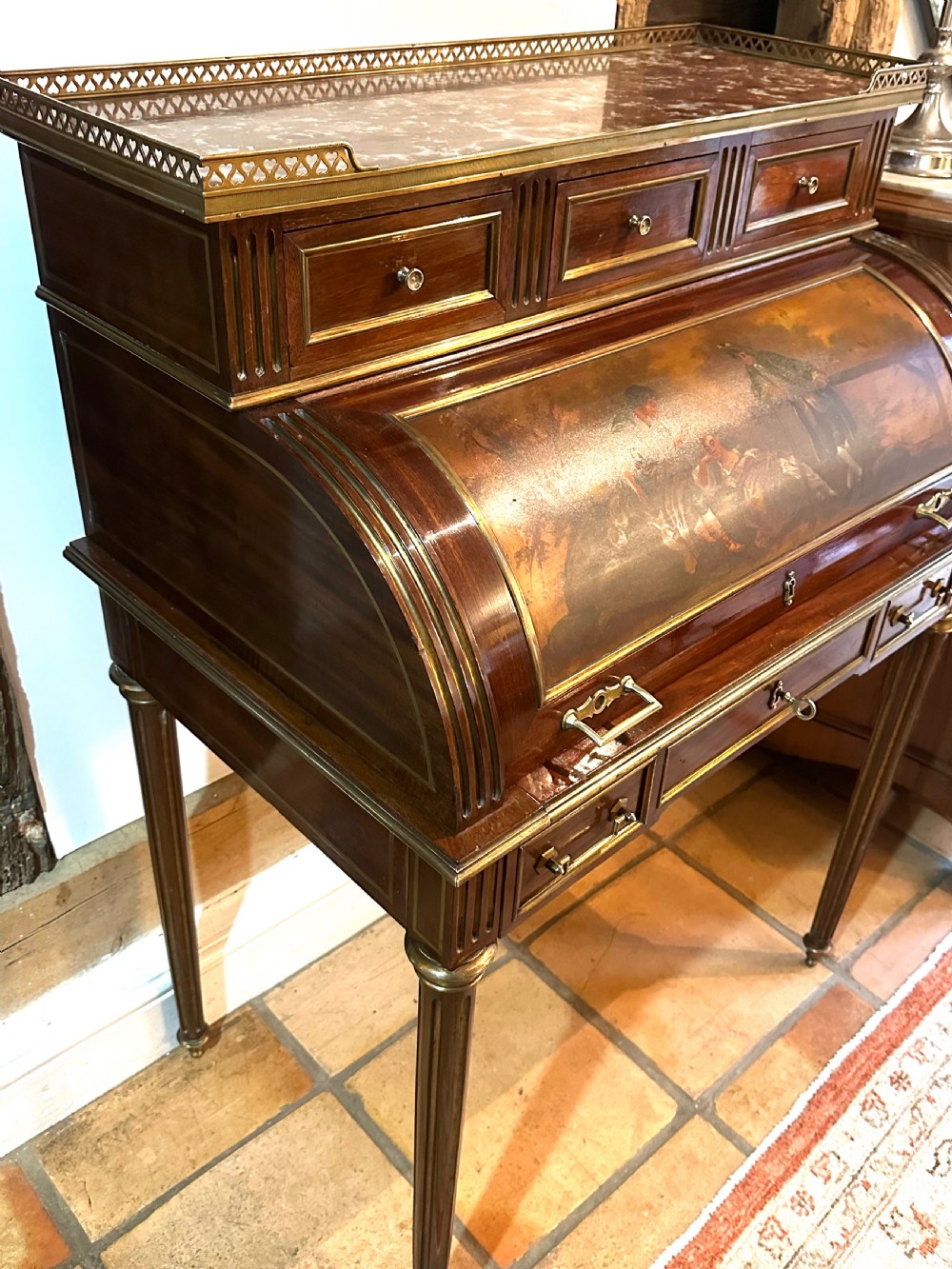 A mahogany French cylinder escritoire featuring a central painted pastoral scene on the roll-top, upper drawer tier, brass mounts, and slender fluted legs. View VI