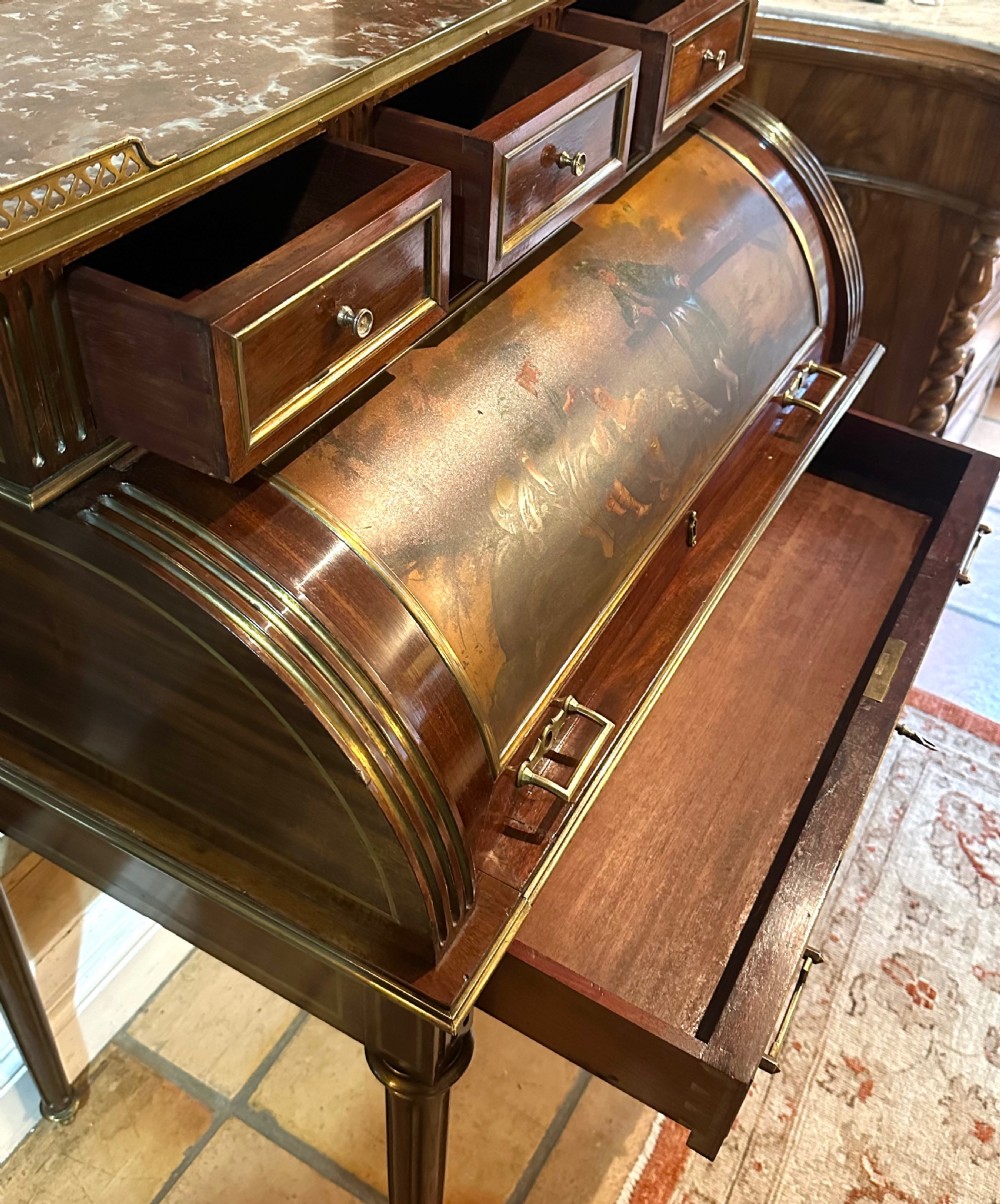 A mahogany French cylinder escritoire featuring a central painted pastoral scene on the roll-top, upper drawer tier, brass mounts, and slender fluted legs. View XIII
