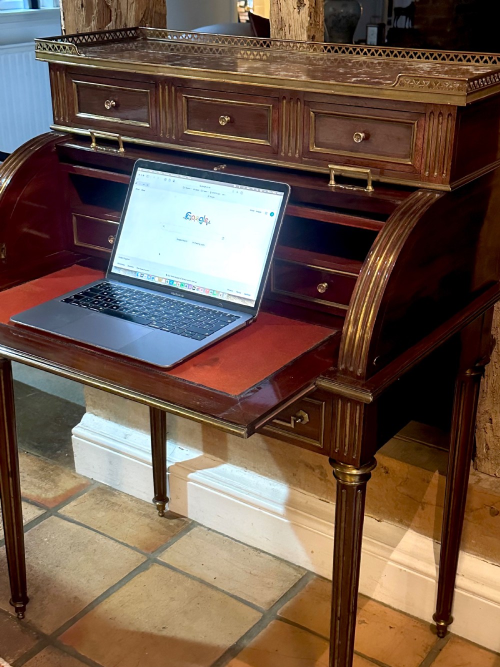 A mahogany French cylinder escritoire featuring a central painted pastoral scene on the roll-top, upper drawer tier, brass mounts, and slender fluted legs. View XVI