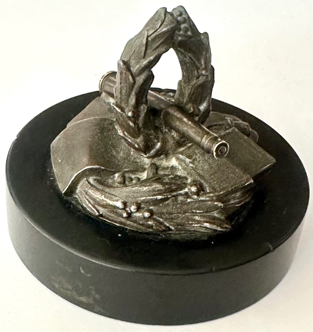 A small bronze military-themed sculpture featuring a laurel wreath, telescope, books, and scroll mounted on a circular black base. View II