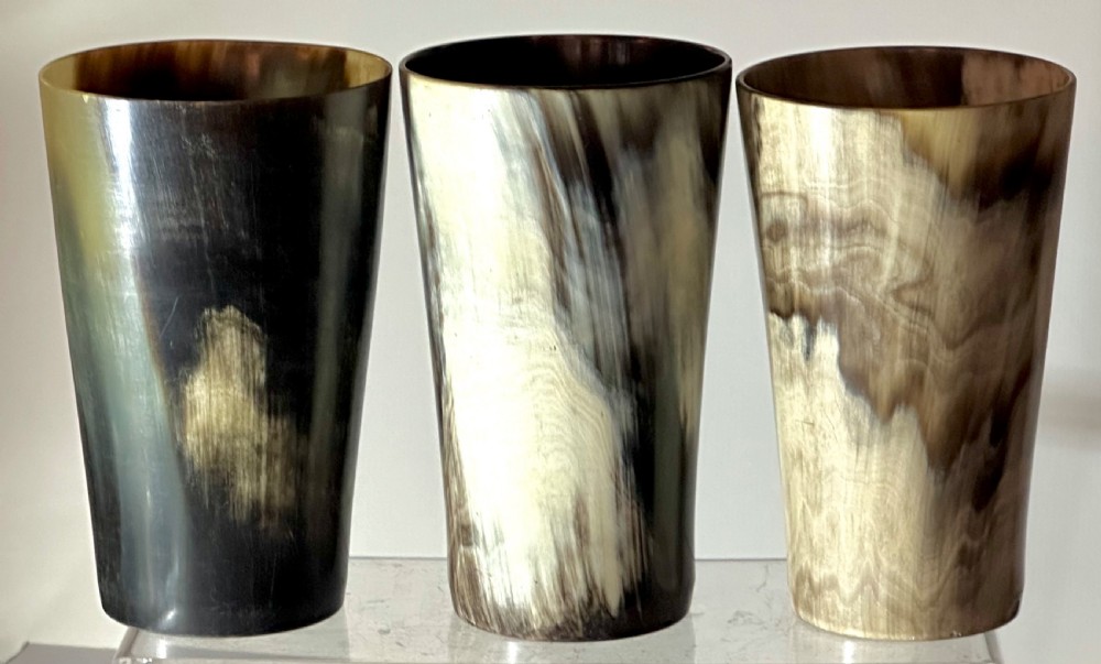 A set of three cylindrical antique drinking beakers made from polished natural horn with variegated cream, amber, and dark brown graining.