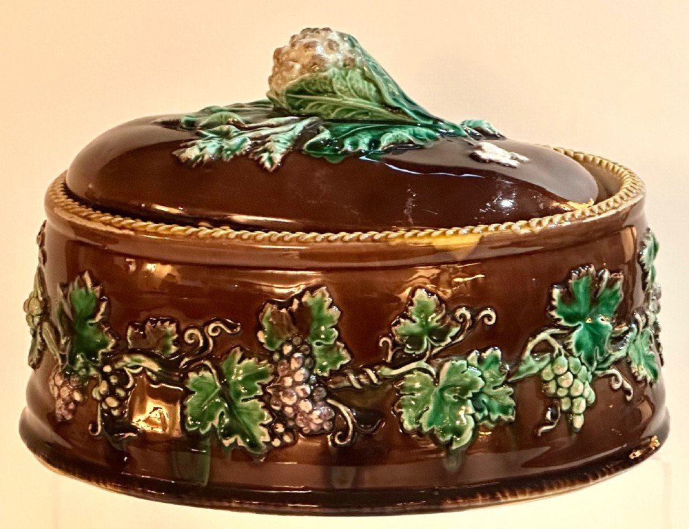 An oval dark brown glazed earthenware tureen featuring relief-moulded green vine leaves and a cauliflower finial on the lid.